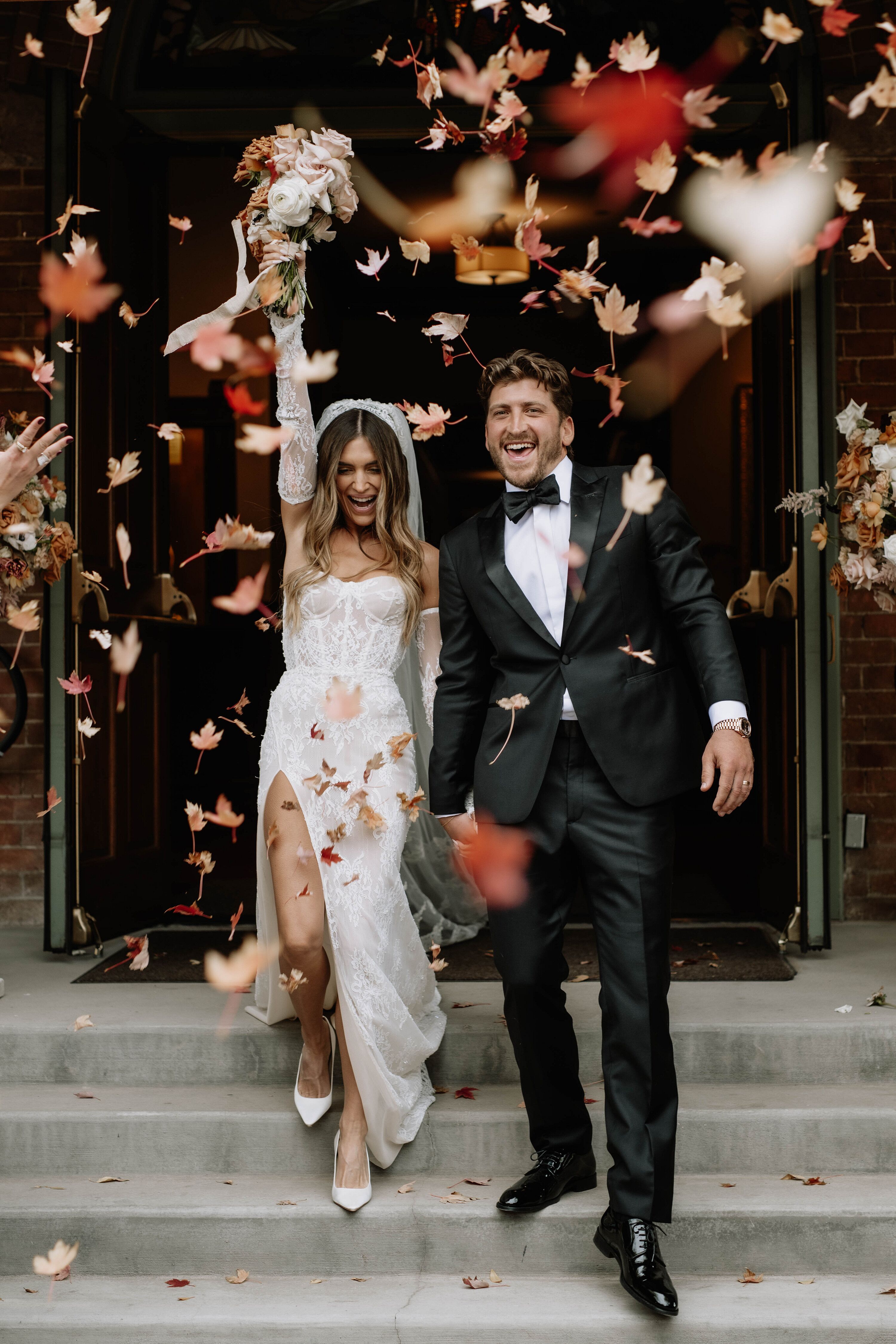Bride in Lace Gown With Slit, Groom in Classic Tuxedo Walking Out of ...