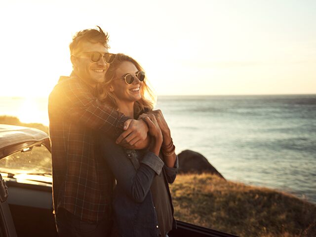 Couple enjoying scenic ocean views while standing against car.