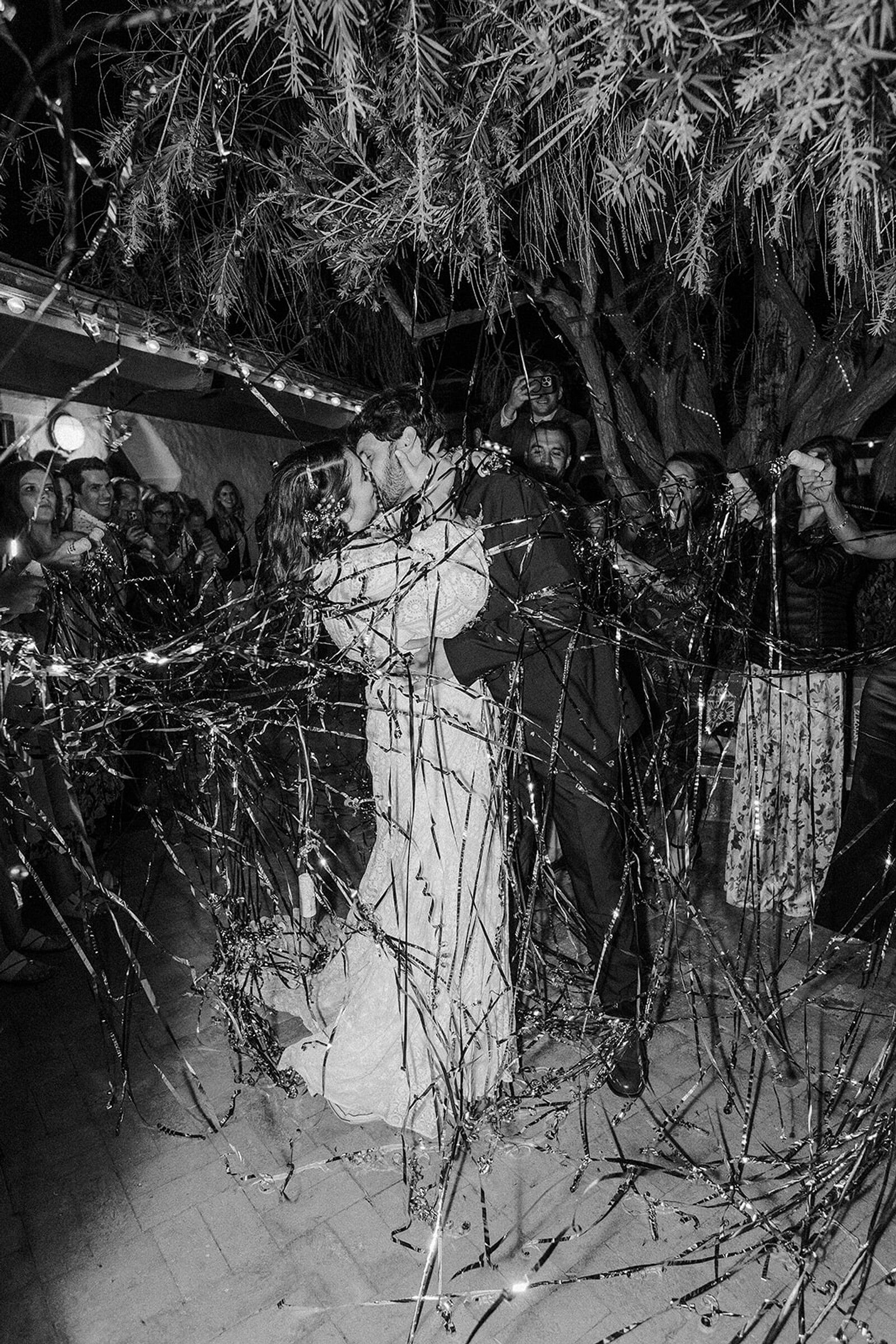 Black-and-White Photo of Bride and Groom Kissing Under Silver Streamers