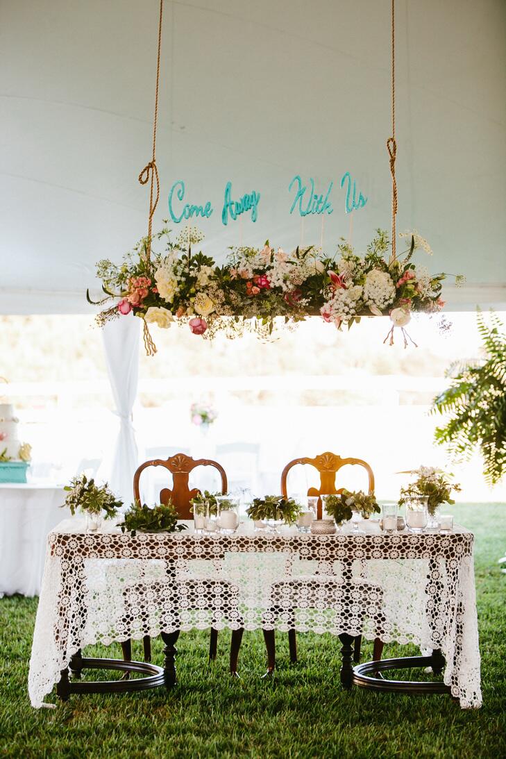 Couple's table with crochet tablecloth and hanging florals and sign