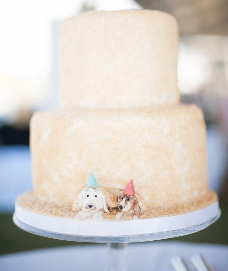 Two dogs peeking out from under a two-tier wedding cake