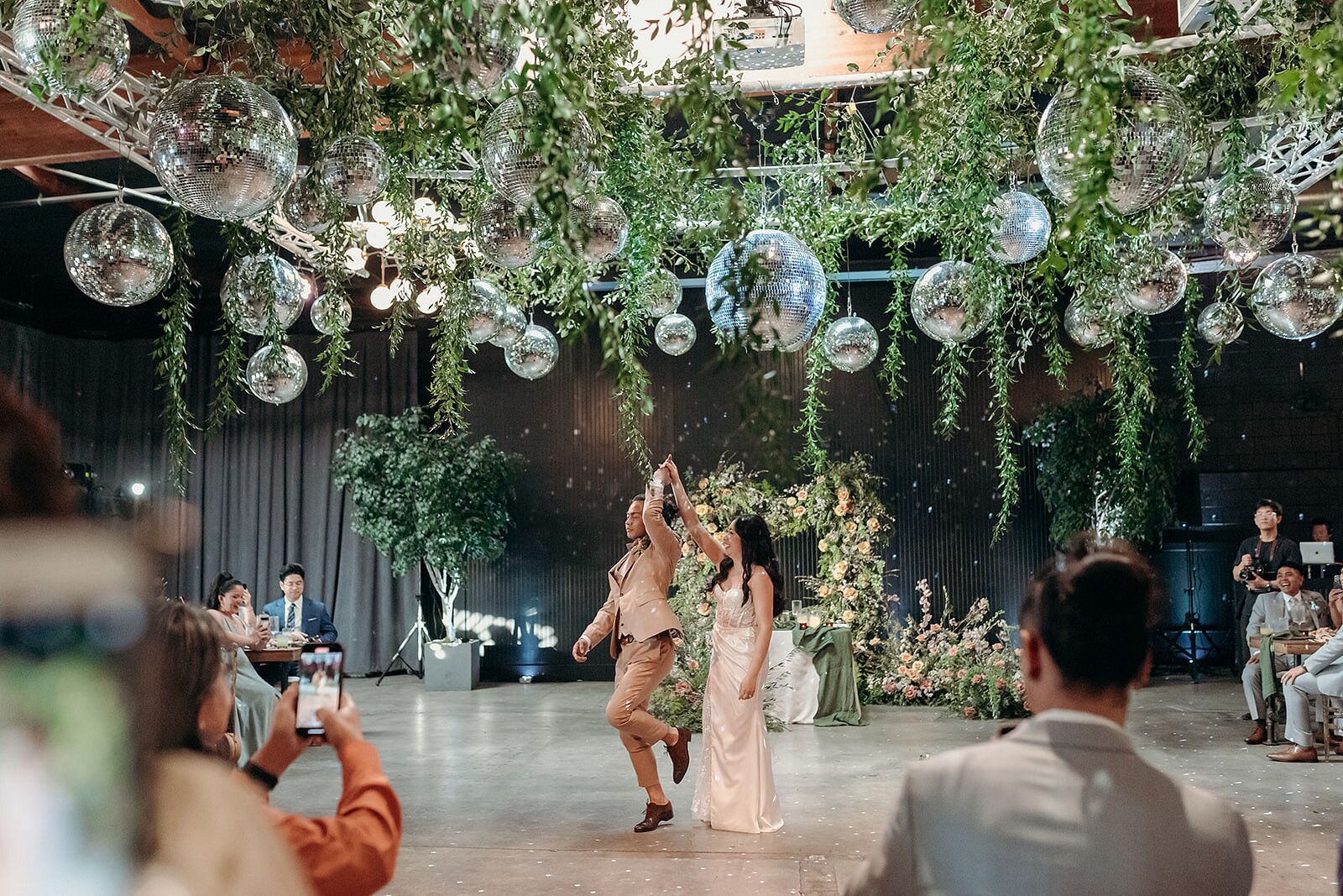 Groom Leading Bride Onto Dance Floor Under Greenery, Disco Ball Hanging 