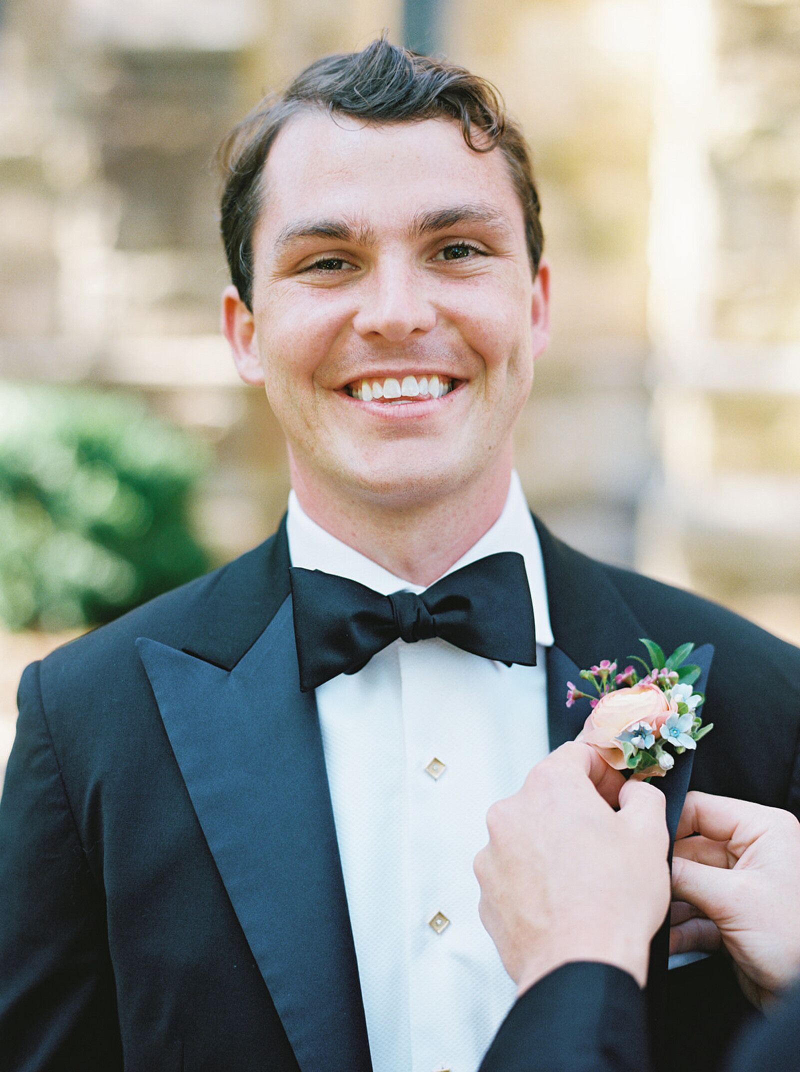 Groom in Classic Black Tux Getting a Colorful Spring Boutonniere Put On