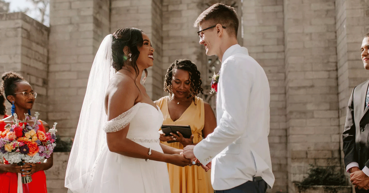 A joyful couple poses under a blooming arch.