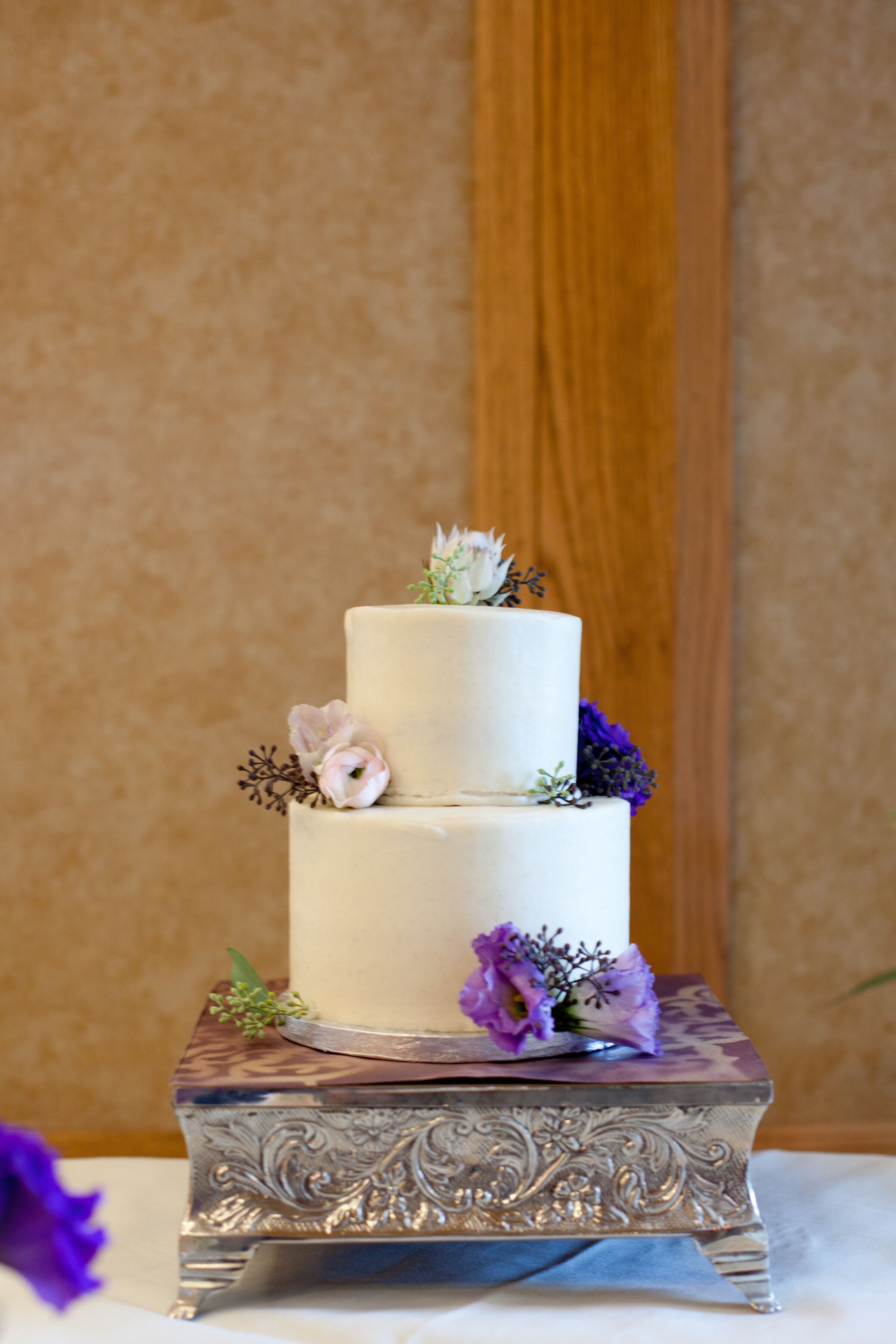 Two Tier Frosted Wedding Cake With Purple Flowers