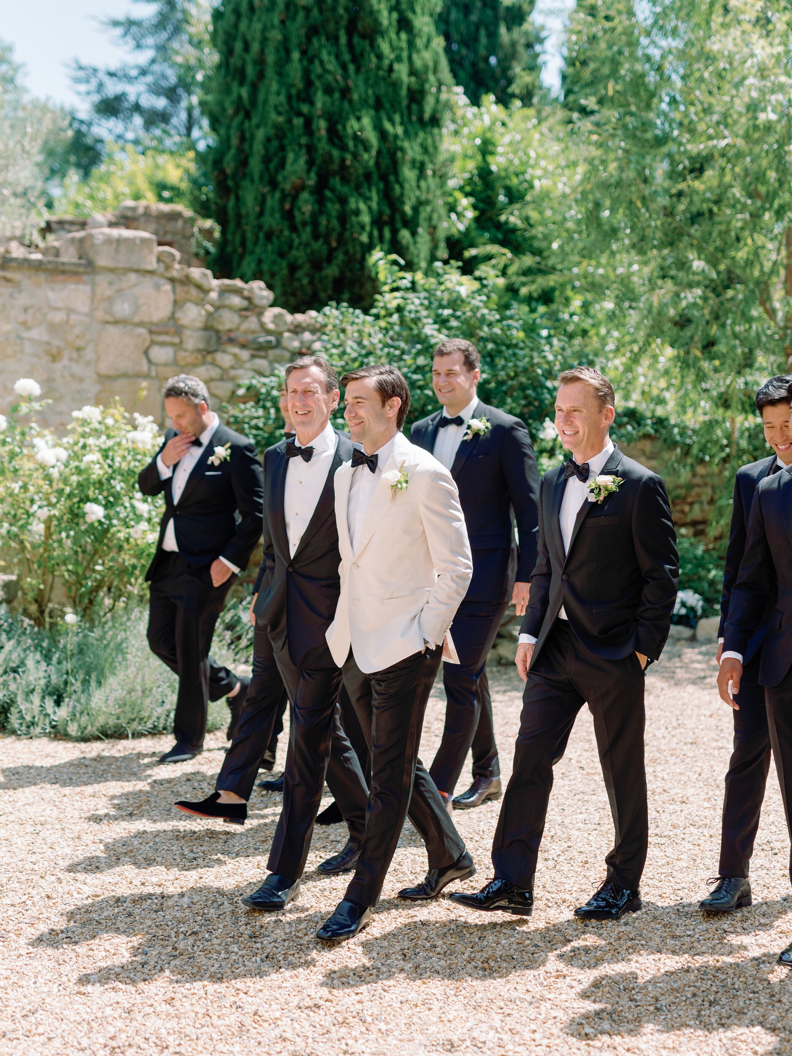 Groom in White Tuxedo Jacket Walking With Groomsmen in Classic Black