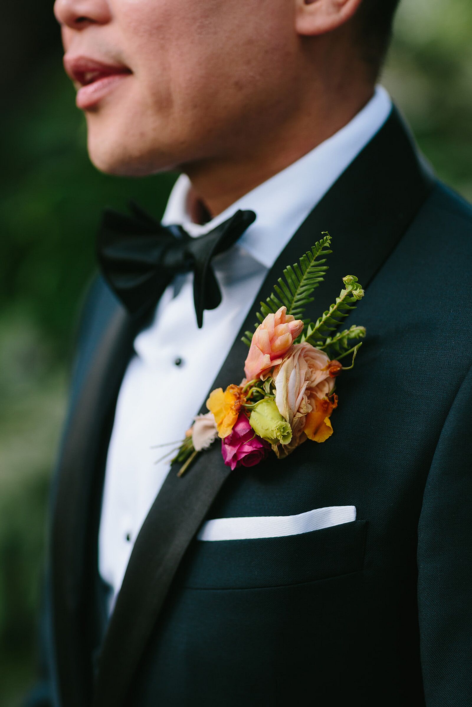 Groom in Black Tuxedo With Colorful, Tropical Boutonniere and Greenery