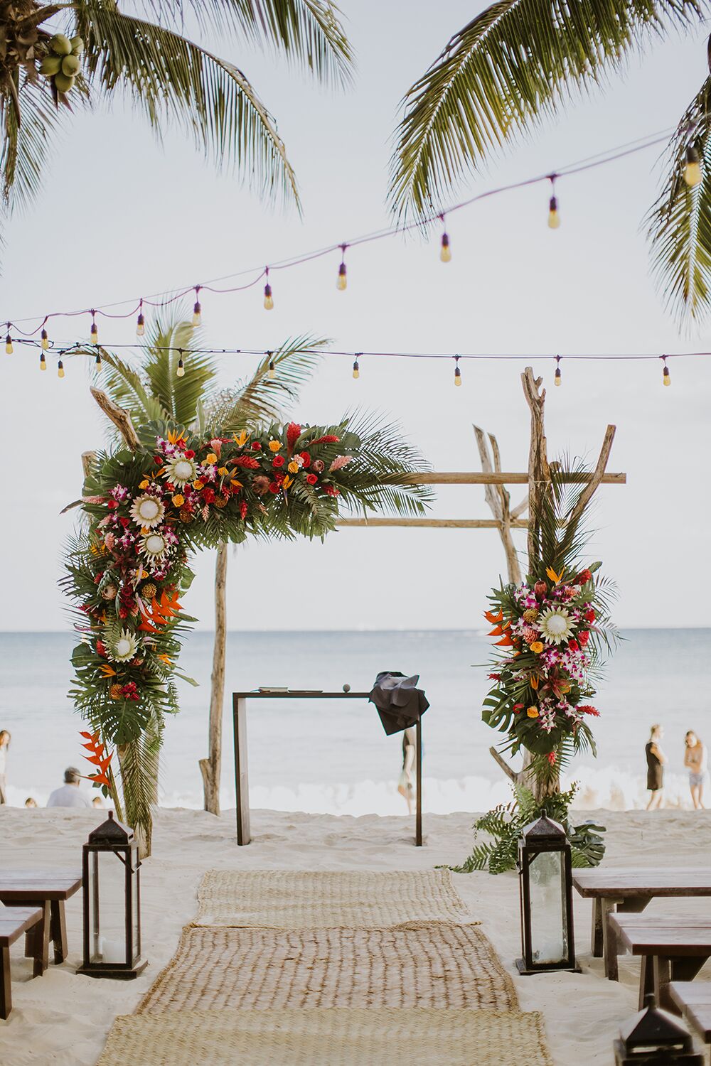 Beach Ceremony Site With Flower Covered Arch And String Lights