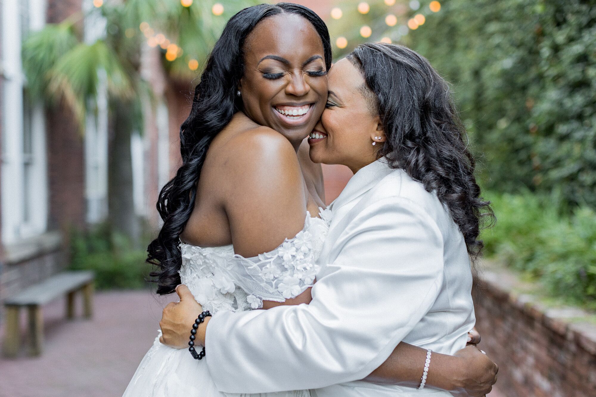 Two Brides in Different White Outfits Embracing With Big Smiles