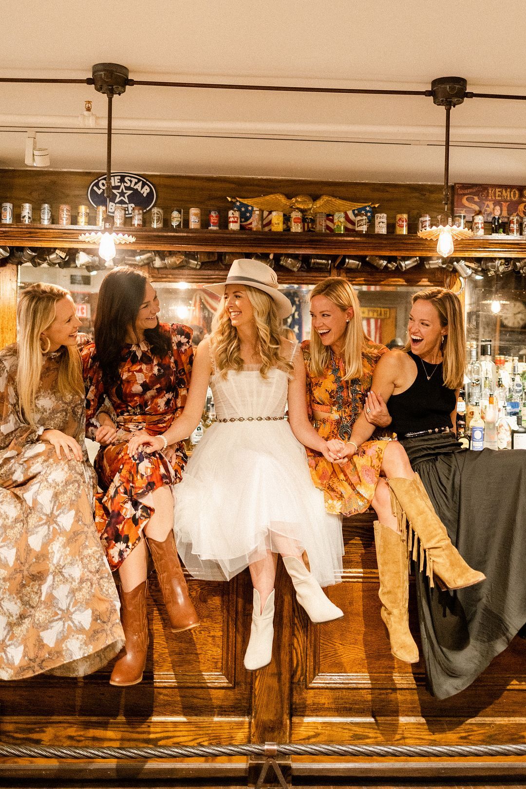 Bride in Short White Dress, Cowboy Boots and Hat With Ladies Sitting on  Western Bar