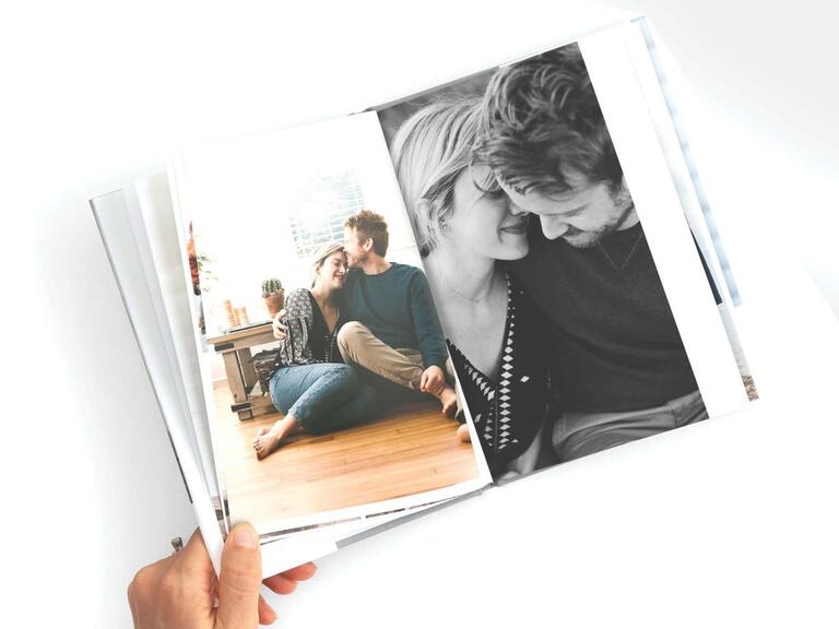 mão da Pessoa foto segurando um livro aberto para mostrar duas fotos de um casal juntos's hand holding photo book open to show two pictures of a couple together